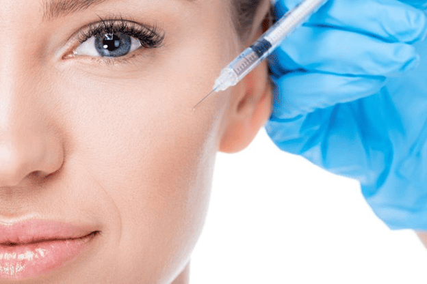 Woman undergoing a facial injectable treatment, with a gloved practitioner positioning a syringe near her outer cheek.